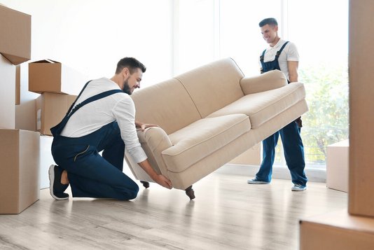 umzug-auszug-einziehen-karton-haus-07 Zwei Umzugshelfer mit Couch